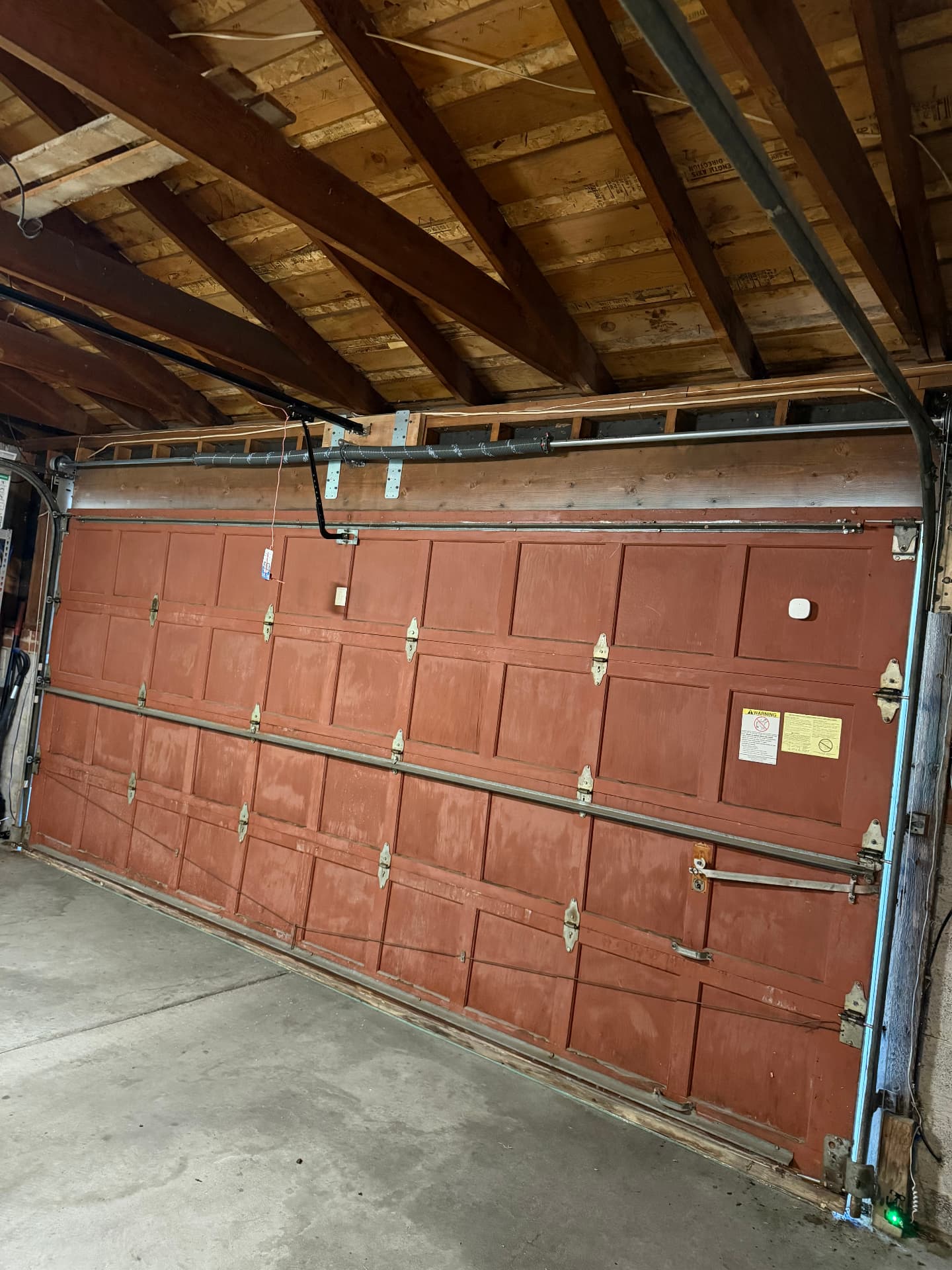 Older wood garage door being serviced inside a detached garage